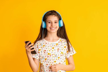 Modern bir akıllı telefonu elinde tutan, kulaklık takan ve müzik dinleyen genç bir kız internetten öğrenip çalmaktan mutlu. Yeni cihazlar ve eğitim uygulamaları tanıtıyordum. Boşluğu kopyala