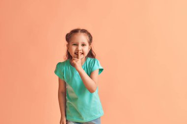 İşaret parmağını ağzına dayayan sevimli küçük bir kızın portresi sarı bir arka planda duruyor. - Çocuk konuşmak istemiyormuş. Sır saklar, sır öğrenir.