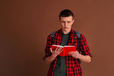 Sırt çantasında kahverengi bir arka planda izole edilmiş kitaplar taşıyan sıradan giyinmiş ciddi bir ergen öğrenci. Lise eğitimi, üniversite konsepti.