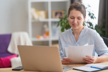 Gülümseyen genç kadın serbest yazar, masa başında bilgisayarla çalışan, faturaları internetten ödeyen, masrafları hesaplayan, mali belgelere bakan..