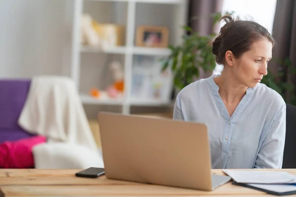 woman sitting at a desk at home working with a computer laptop is tired and bored at office work. unmotivated lazy brown-haired woman feels sleepy at a boring job and lack of sleep