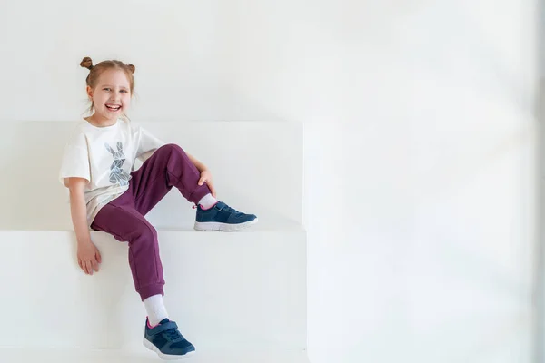 一个穿着时髦衣服的快乐小女孩笑了 并在工作室的白墙前摆姿势 为儿童服装 情感儿童 时尚儿童形象做广告的概念 复制空间 — 图库照片