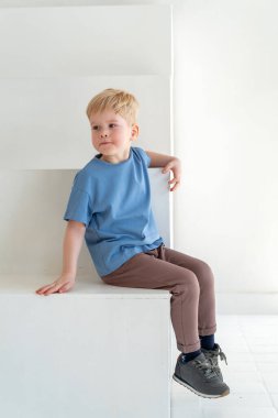 Şık giyinmiş, gülümseyen, beyaz duvar stüdyosunun önünde poz veren küçük mutlu sarışın çocuk. Çocuk kıyafetlerinin reklamını yapma konsepti, çocuğun duygusallığı. Boşluğu kopyala