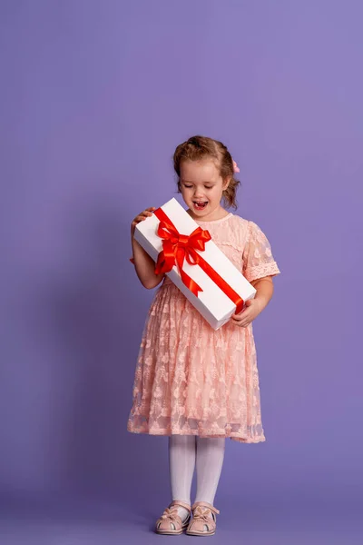 可爱的小女孩 带着紫色背景的红丝带礼品盒 小孩的生日 一个快乐的孩子手里拿着一份礼物 一份生日礼物 给予和接受的概念 — 图库照片
