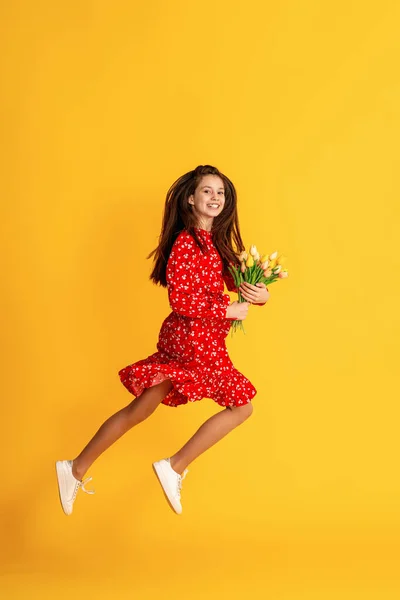 可爱迷人的梦幻少女 与花束郁金香 红色衣服与花卉印 躺在黄色工作室的背景 白种人的黑发在背景墙上跳跃 复制空间 — 图库照片