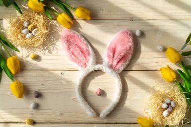 Paskalya bayramı. Yuvalarda yumurtalar, sarı laleler ve doğal güneş ışığı olan açık tahta bir masada tavşan kulakları. Kopya alanı olan tebrik kartı arkaplanı.