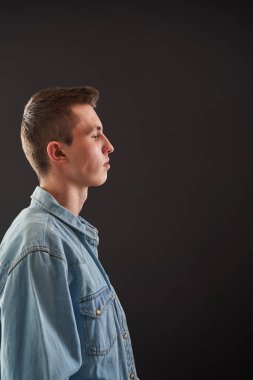 Sakin, ciddi bir gencin portresi, bir öğrenci, serbest stil kıyafetler giymiş, stüdyoda siyah bir arka planda duruyor. Geçiş yaşı