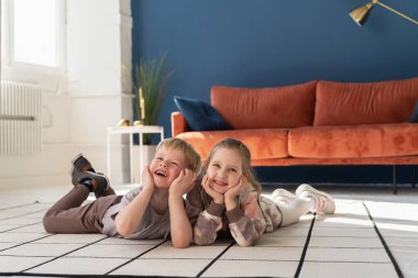 Küçük mutlu beyaz çocuklar, 5 yaşında bir oğlan ve kız, rahat kıyafetler giyip, halıya uzanıp birbirleriyle iletişim kuruyorlar. Mutlu bir çocukluk. Reklam.