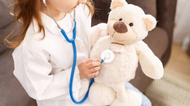Gözlüklü, beyaz üniformalı beyaz bir kız oyuncak ayıyı tedavi ediyor, doktorculuk oynuyor. Mutlu bir çocuk veteriner kliniğinde oyuncağı inceleyen bir doktor gibi davranır..