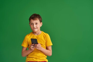 İlgili çocuk elinde yeni bir akıllı telefon tutuyor, yeşil arka planda önünde duruyor. Öğrenci cihaz bağımlısı, mobil aygıtla oyun oynuyor