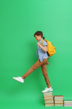 Pozitif 8 yaşında, bol elbiseli, sırt çantalı bir çocuk yeşil arka planda kitap basamaklarına tırmanıyor. Okuma arzusu. Başarılı bir bilgi edinme. Reklam. kitapçı