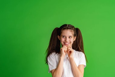 Beyaz tişörtlü, kara kara düşünen 10 yaşında bir kız yeşil arka planda çenesini tutuyor. Çocuk kafasını çevirir ve kararını düşünür, doğru cevabı yansıtır. kopyalama alanı