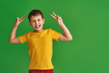 Sarı tişörtlü, mutlu ve muzaffer bir çocuk portresi. Zafer ve barışı simgeliyor. Gülümsüyor, Ziyaretçi işareti yapıyor.