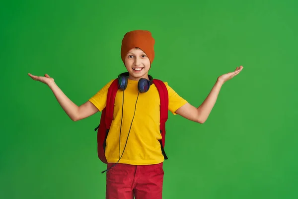 身穿休闲装 耳机和背包的快乐的白人学童 站在绿色的背景上 男孩把手伸向不同的方向 回学校去概念教育 — 图库照片