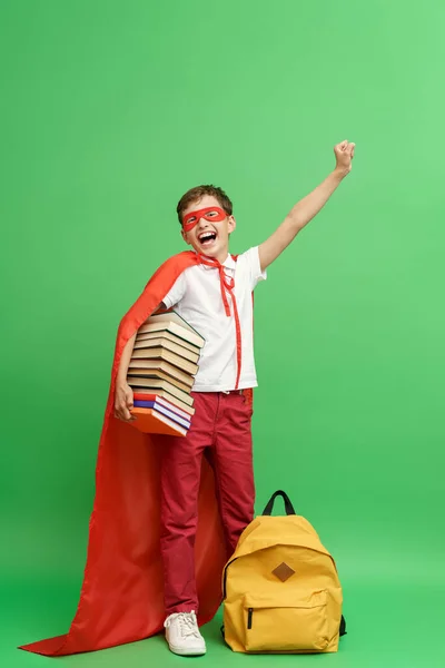 幸せな感情的な子供 スーパーヒーローの衣装に身を包んだ バックパックで 彼の手に本のスタックを保持し 熱狂的に笑って 学校の知識のために努力する知識に進む — ストック写真