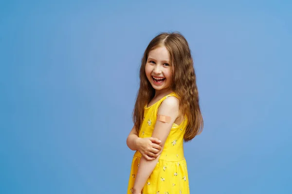快乐微笑接种疫苗小女孩在注射Covid 19疫苗后 用补丁展示她的手 呈现蓝色背景 防治结肠病毒疫苗的广告 — 图库照片