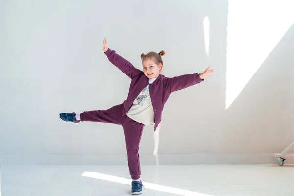 身穿时髦服装的快乐小女孩微笑着 摆出姿势 爬上了工作室的白墙 儿童服装广告的概念 情感儿童 动态形象 — 图库照片