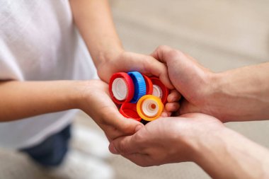 Çocukların ve erkeklerin elleri plastik kapakları tutar. Bir baba ve çocuğu geri dönüşüm için kapakları topluyor. Çevre koruma