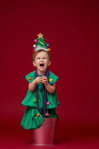 身穿圣诞树装束的小女孩站在红色背景的水桶里 那孩子很不高兴 哭哭啼啼 很不高兴 — 图库照片