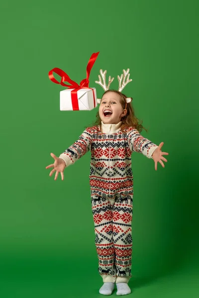 驯鹿鹿角上快乐的女婴在绿色背景下抓起礼品盒 儿童羊毛衫 冬季装饰跑步和跳跃在绿色背景下充分成长 动态图像 — 图库照片