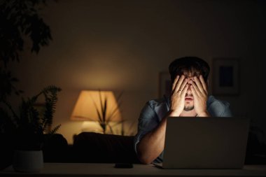 Yorgun erkek işadamı geceleri evde dizüstü bilgisayarla çalışıyor, evde çalışıyor, internetten çalışıyor. İnternet bağımlılığı ya da geç saatlere kadar çalışan biri. Korkmuş bir adam evinde geç saatlere kadar çalışıyor.