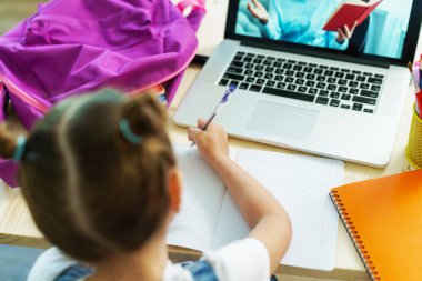 Küçük kız öğretmeniyle video görüşmesi yapmak için dizüstü bilgisayar kullanıyor. Çocuk uzaktan öğrendiği için mutlu. Öğrenci kız bilgi almaktan mutlu. E-Eğitim. Seçici bir şekilde ele odaklan. en üstteki görünüm