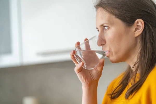 若い女性は台所で水を飲む 女は喉が渇き暑い日に喉が渇く 水バランスに準拠しています — ストック写真