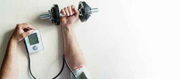 Checking blood pressure when doing sports. A person with dumbbells in his hand measures blood pressure. Top view. Close-up