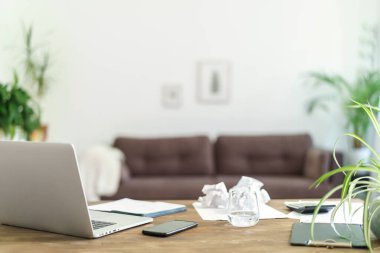 Dizüstü bilgisayar, cam su ve belgeler arka plandaki parlak odanın karşısında duruyor. Arka plan bulanık. Evdeki işyerinde. Uzaktan kumanda. Serbest çalışan biri. Coronavirus karantinası. uzak çalışma konsepti.