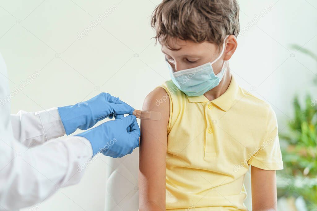 doctor gives a child in a medical mask an injection in the shoulder. Vaccination of children against coronavirus. The vaccine against Covid-19