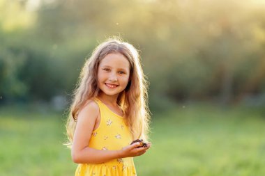 Küçük meraklı kız 5 yaşında, elinde büyük kara kurbağası, elinde kurbağa, temiz havadayken. Çocuk merakla ve ilgiyle amfibik hayvana bakıyor. Bebek kurbağayı öpmek istiyor..