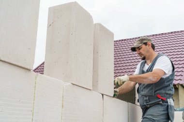 Tulumlu genç cesur erkek inşaat işçisi inşaat sahasına beton bloklar yerleştiriyor. Yapıştırıcı üzerine yüksek kaliteli bloklar döşemek, bir ev inşa etmek.. Boşluğu kopyala