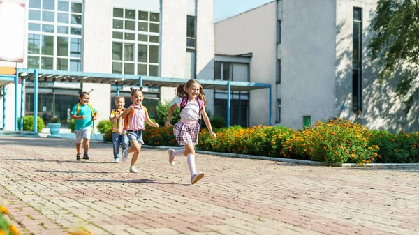 group of school children with backpacks run out of school, after the end of classes. Classmates, school friends. The beginning of holidays. The end of quarantine. Back to school.