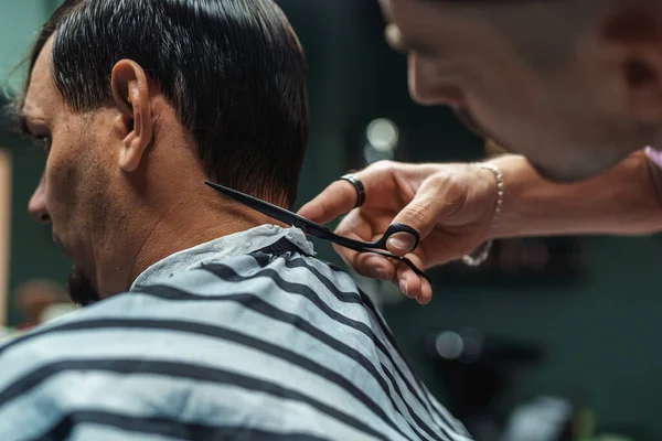 young barber guy gives a haircut to a bearded man sitting in a chair in a barbershop. A man cuts his hair with scissors and a comb. Men\'s haircuts and beard shaving. Haircut and edging of eyebrows.