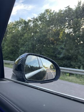 Yeşil bir ormanda uzanan boş bir yolu gösteren bir arabanın yan aynasına bak. Seyahat, seyahat, hareket, özgürlük ve yön kavramı. Doğal ışık, yaz atmosferi, kopyalama alanı.