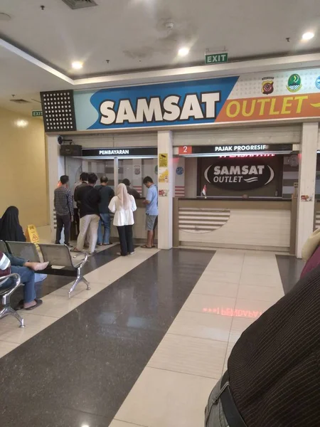 Samsat 'ın hareketli bir fotoğrafı kapalı bir yerde, muhtemelen bir alışveriş merkezi ya da kamu hizmeti merkezinde, insanlar ödeme ve ilerici vergi hizmetleri için kuyruğa giriyor.