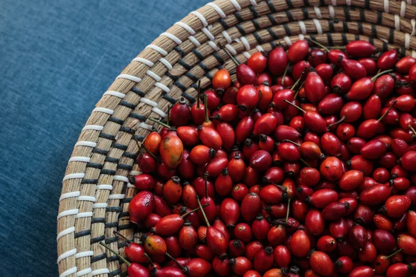 Koyu mavi kumaş bir yüzeye yerleştirilmiş parlak kırmızı gül kalçalarıyla dolu bir sepet. Canlı renk kontrastı meyvelerin doğal güzelliğini vurgular ve sakin ve dengeli bir kompozisyon yaratır..