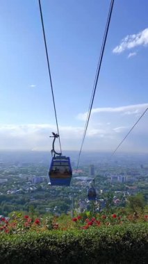 Almaty, Kok-Tobe, Kazakistan - 17 Ağustos 2025: Güneşli bir günde şehrin ve dağların panoramik manzarasına karşı mavi bir teleferik.. 
