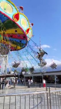 Almaty, Kazakistan - 17 Ekim 2025: Parlak renkli bir atlıkarınca zinciri, güneşli bir günde bir lunaparkta açık mavi gökyüzü ve dağların arkasında hızla hareket ediyor.