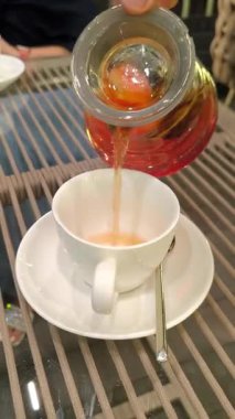 Bir el, portakal kırmızısı sıcak çayı cam çaydanlıktan kar beyazı porselen bir fincana döker..