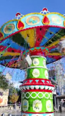 Almaty, Kazakistan - 17 Ekim 2025: Parlak renkli bir atlıkarınca zinciri, güneşli bir günde bir lunaparkta açık mavi gökyüzü ve dağların arkasında hızla hareket ediyor.