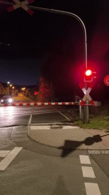 Gece çekilen dikey bir video demiryolu geçidinde bariyer kurmanın dinamik sürecini gösteriyor. Önce bariyer indirilir ve trafik ışığı kırmızıya döner. Sonra bariyer yükselmeye başlar ve kırmızı ışık söner..