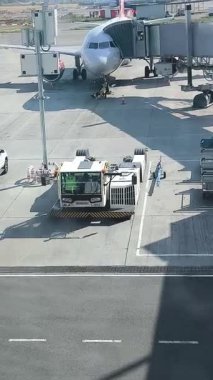 Almaty, Kazakistan - 22 Ağustos 2025: Jet köprüsüne yanaşmış yolcu uçağını çekmek için bekleyen sarı çizgili bir havaalanı.