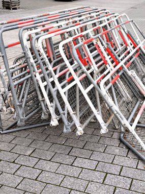 Bir yığın ağır, geçici metal bariyer ya da kalabalığı kontrol eden eskrim, gri bir kaldırım levhasının üzerinde, beklenti, düzen ve geçici kısıtlama duygusu taşır..