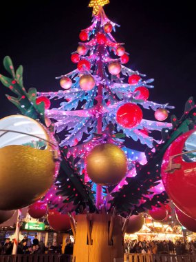 Birçok kırmızı ve pembe ışık ve insanların binmesi için kamara şeklinde büyük kırmızı ve altın toplarla süslenmiş modern, gelecekçi bir Noel ağacı..