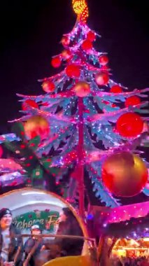 Halle-Saale, Almanya - 6 Aralık 2025: İnsanların binmesi için kabin şeklinde kırmızı ve pembe ışıklar ve büyük kırmızı ve altın toplarla süslenmiş modern, fütürist bir Noel ağacı.