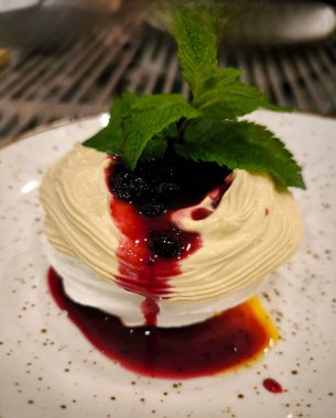An exquisite meringue dessert with a delicate cream, drizzled with berry syrup, and garnished with a sprig of fresh mint. Serve on a plate.