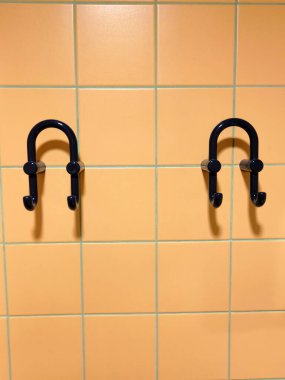 Minimalist mavi ilmek askıları turuncu kare karolarla kaplı bir duvara monte edilmiş.