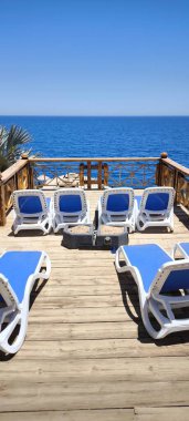 Lüks otellerin, ahşap güvertenin, rahat mavi şezlongların, ahşap korkulukların ve güneşli bir günde okyanusun panoramik manzarasının manzarası.