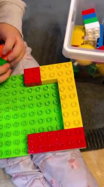 Kırmızı, sarı ve yeşil bloklardan bir yapı inşa eden bir çocuğun yakın çekimi. Bu eğitim oyunu çocuklarda iyi motor becerileri ve yaratıcı düşünmeyi teşvik eder..